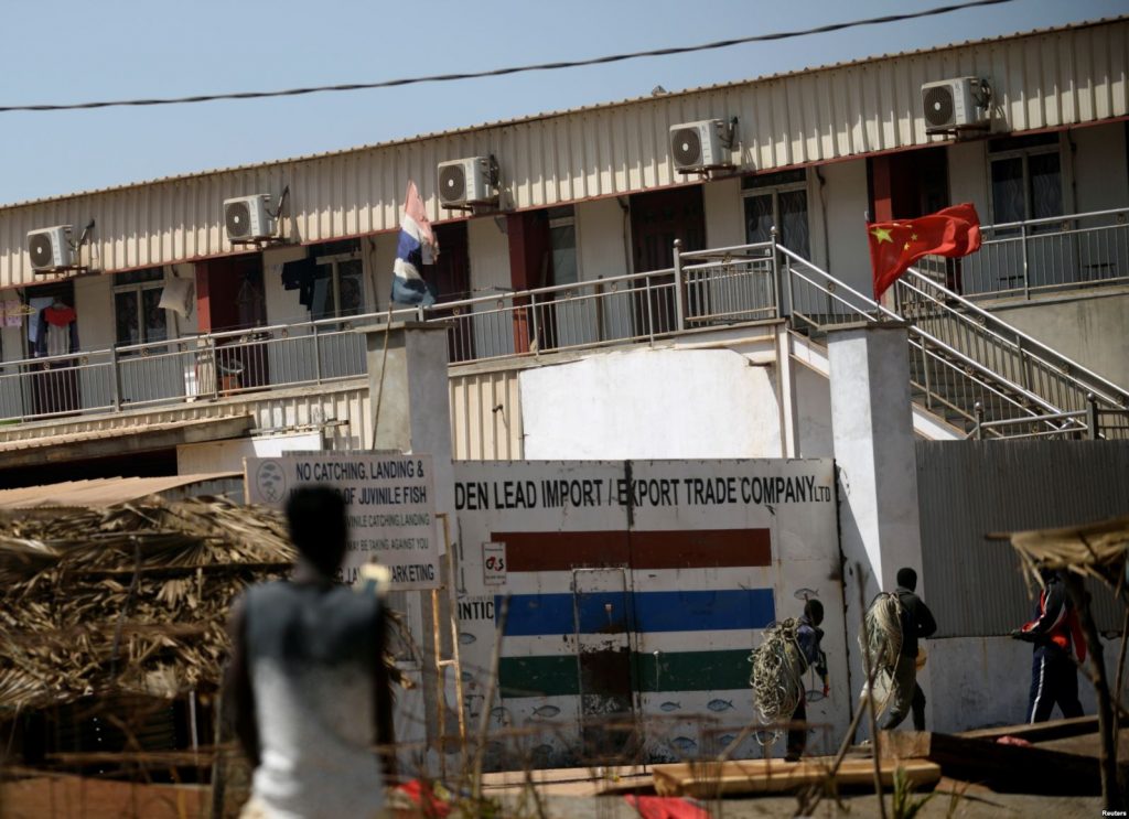 Men carry fishing ropes outside the gates of the Chinese-owned Golden Lead fishmeal factory in the fishing village of Gunjur, Gambia